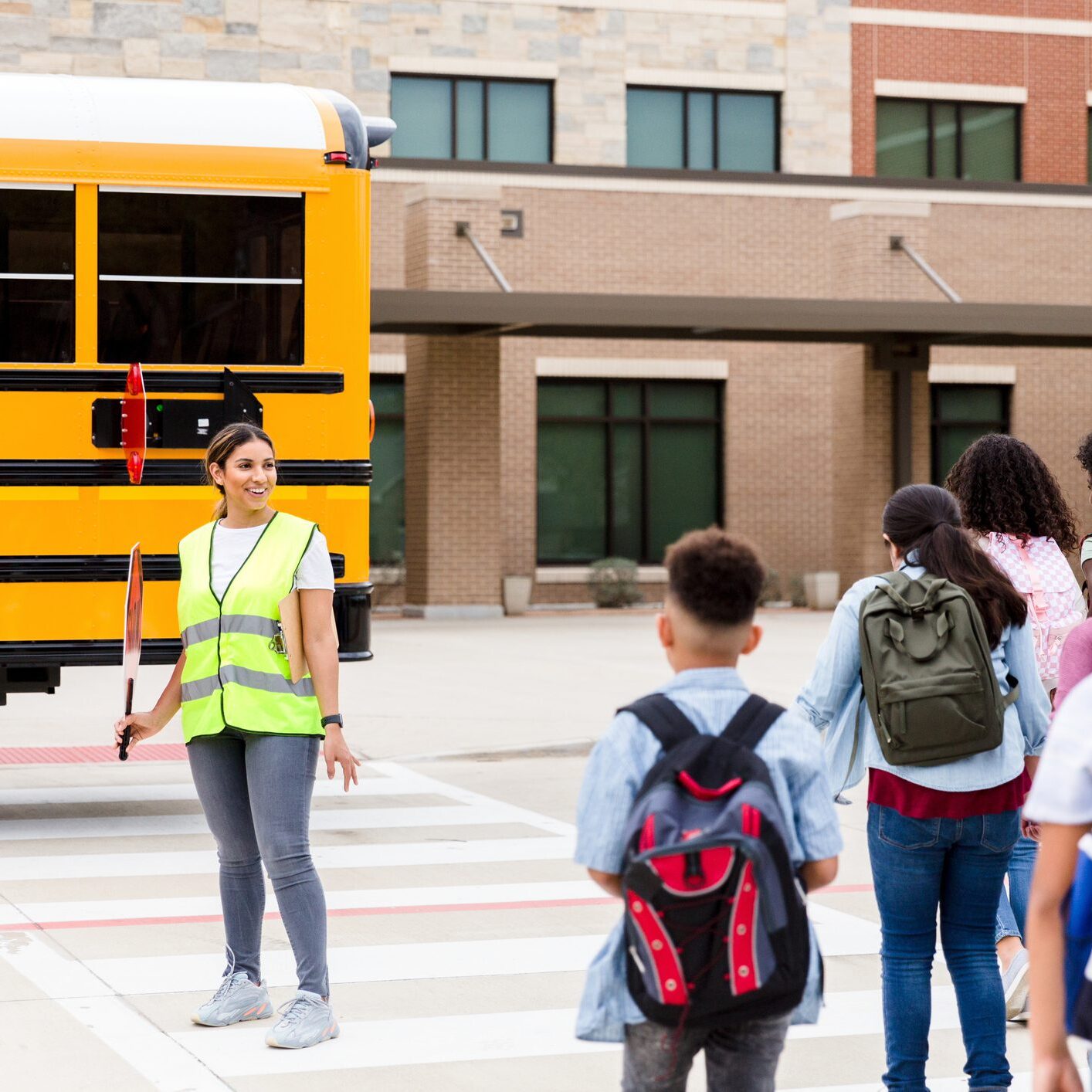 As the school children head toward the building on the crosswalk, the crossing guard greets them with a smile.
