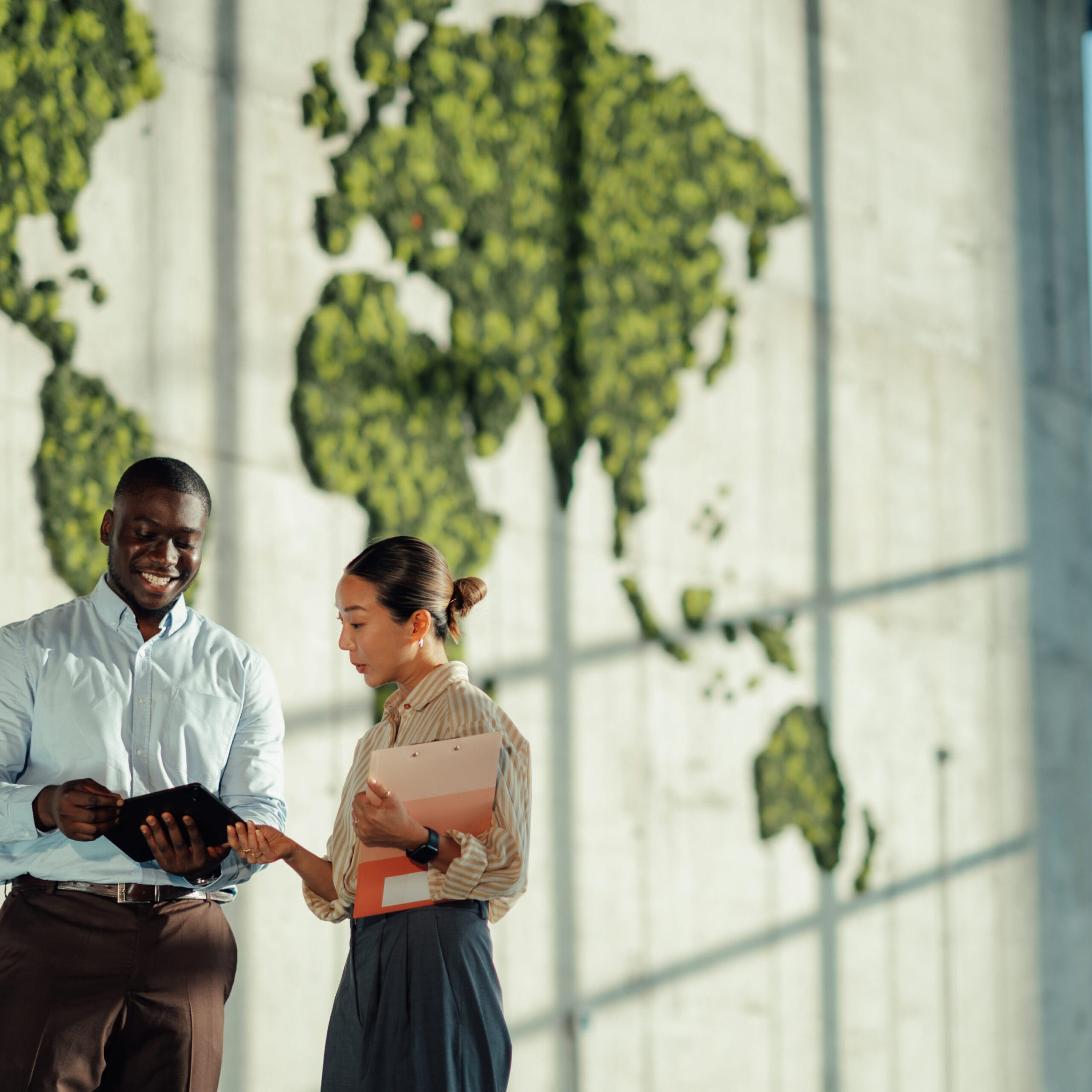 Two business colleagues are discussing global strategies in a modern office with a large green world map