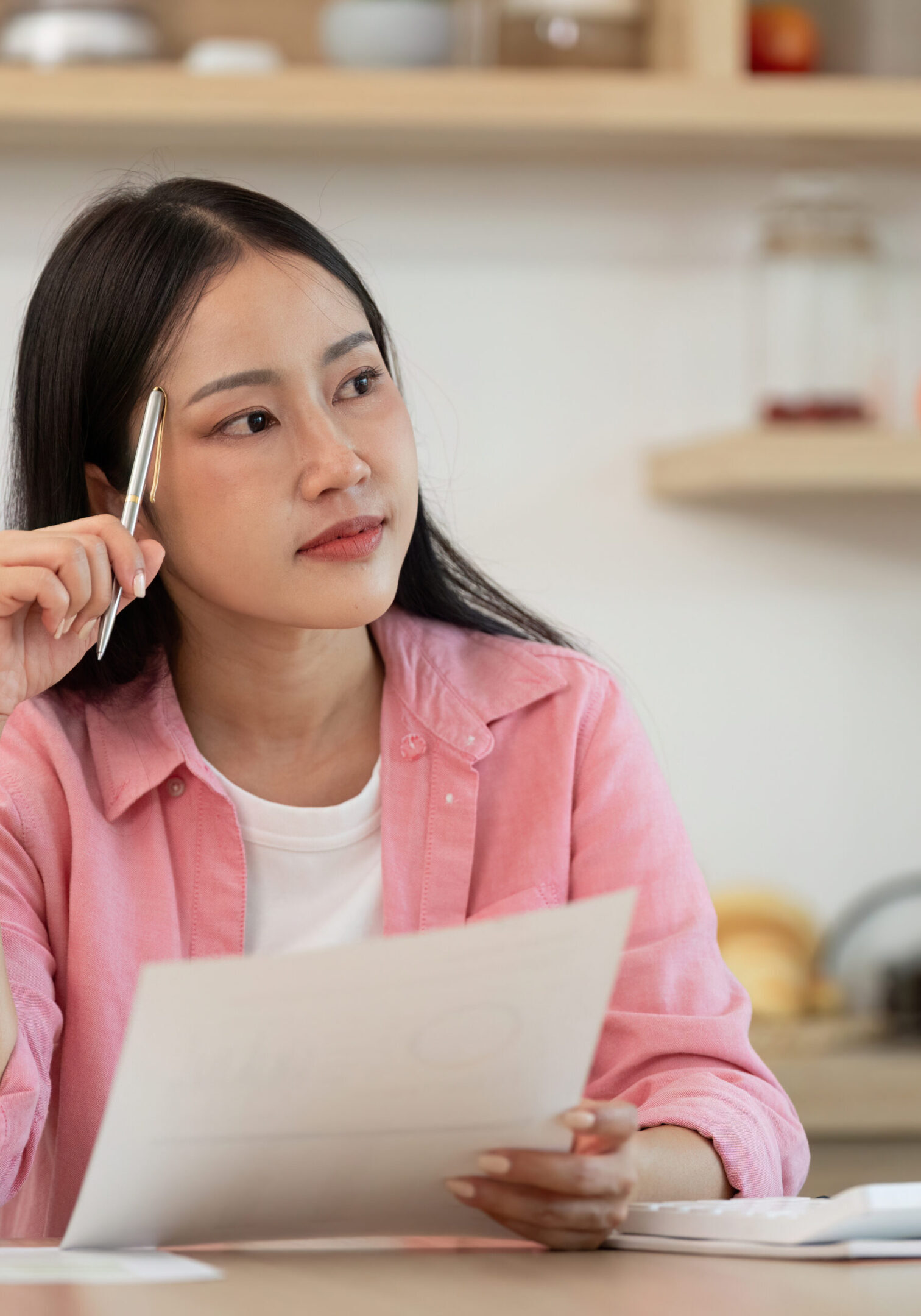 A woman contemplates her documents in a cozy kitchen, reflecting on her work and planning for future tasks.